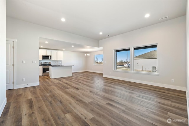 unfurnished living room with an inviting chandelier, dark hardwood / wood-style flooring, and sink