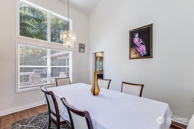 dining room featuring a towering ceiling, dark wood-type flooring, and an inviting chandelier