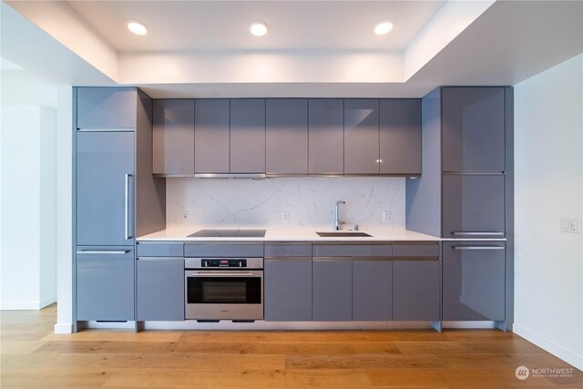 kitchen with light hardwood / wood-style floors, oven, backsplash, and sink