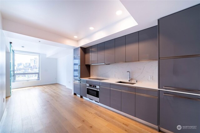 kitchen with black electric cooktop, stainless steel oven, backsplash, light hardwood / wood-style floors, and sink