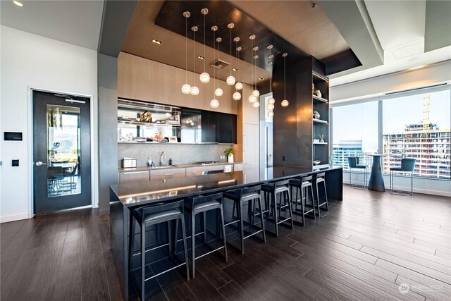 kitchen with a breakfast bar area, hanging light fixtures, a kitchen island, decorative backsplash, and dark hardwood / wood-style flooring