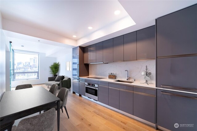 kitchen featuring black electric stovetop, oven, sink, light hardwood / wood-style flooring, and backsplash