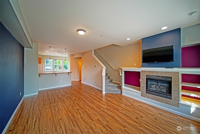 unfurnished living room with a tiled fireplace and hardwood / wood-style flooring