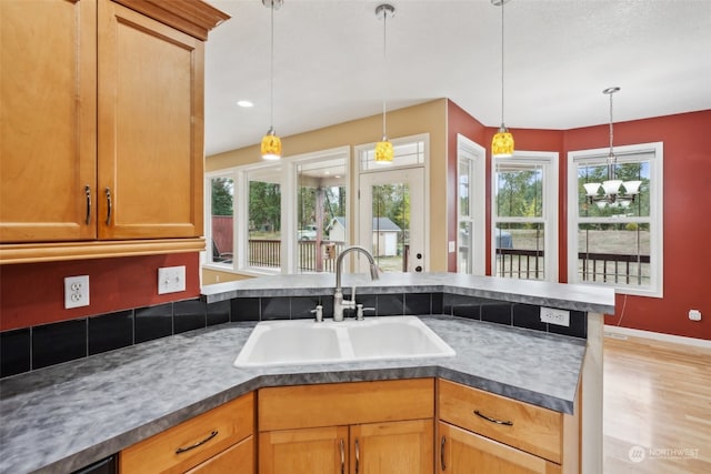 kitchen with decorative light fixtures, light wood-type flooring, sink, and a wealth of natural light