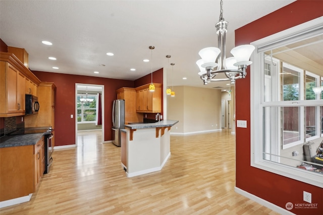 kitchen with hanging light fixtures, a breakfast bar area, light wood-type flooring, black appliances, and a notable chandelier