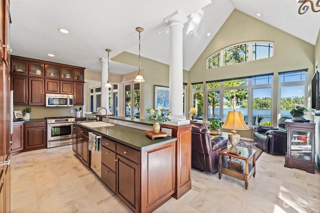 kitchen with a sink, open floor plan, appliances with stainless steel finishes, dark countertops, and decorative columns