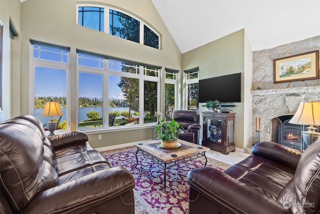 living room featuring a stone fireplace, a towering ceiling, and a water view