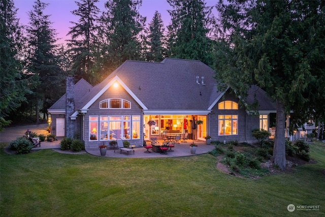 back house at dusk with a patio area and a lawn