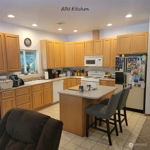 kitchen featuring a kitchen bar, light brown cabinetry, white appliances, sink, and a kitchen island