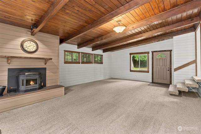 unfurnished living room featuring wood walls, a wood stove, wooden ceiling, carpet flooring, and vaulted ceiling with beams