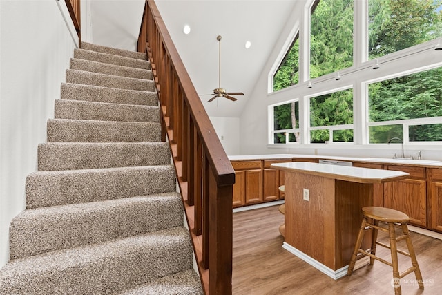 stairs with ceiling fan, sink, a healthy amount of sunlight, high vaulted ceiling, and hardwood / wood-style flooring