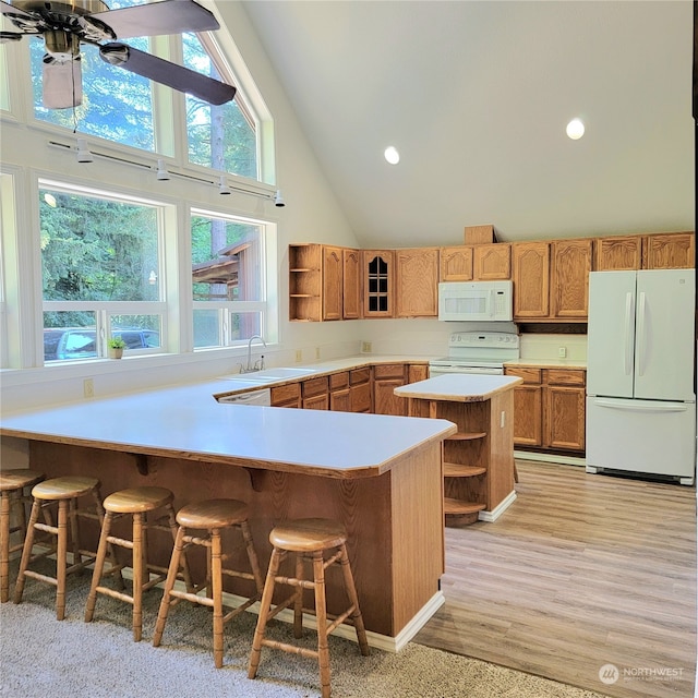 kitchen featuring a kitchen breakfast bar, white appliances, kitchen peninsula, and high vaulted ceiling