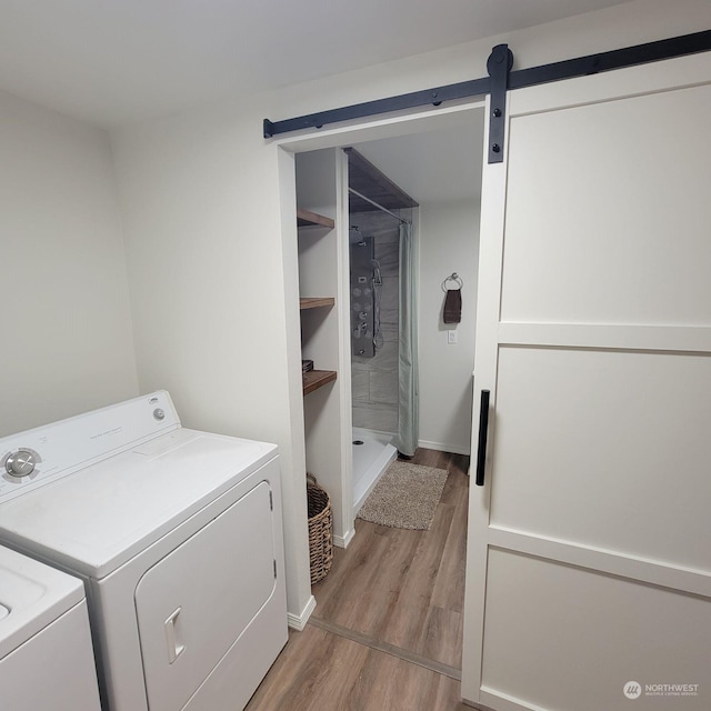 laundry area with a barn door, washing machine and dryer, and light hardwood / wood-style flooring