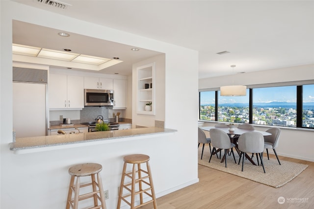 kitchen with appliances with stainless steel finishes, pendant lighting, kitchen peninsula, light hardwood / wood-style floors, and white cabinetry