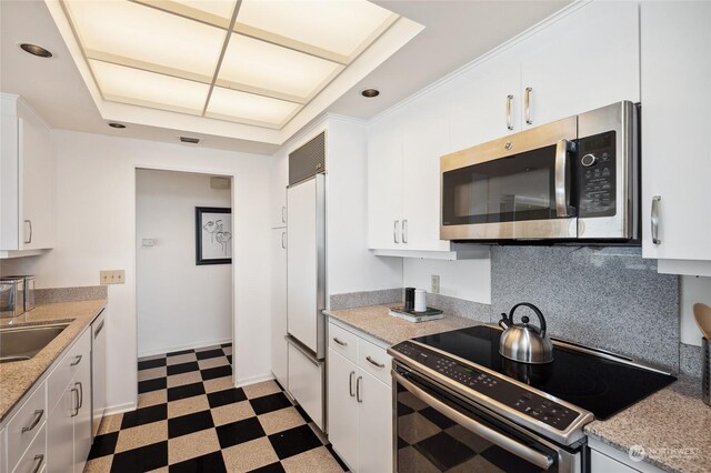 kitchen with electric stove, tasteful backsplash, white cabinets, paneled built in fridge, and light tile patterned flooring