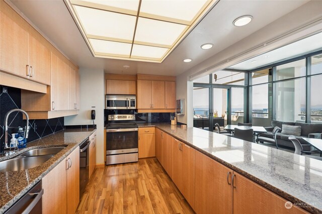 kitchen with stone counters, tasteful backsplash, light wood-type flooring, and stainless steel appliances