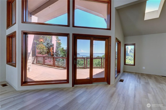 doorway with light hardwood / wood-style floors, high vaulted ceiling, and a skylight