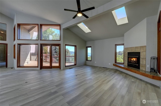 unfurnished living room with high vaulted ceiling, light wood-type flooring, ceiling fan, a tile fireplace, and beam ceiling