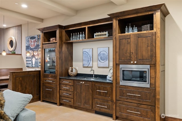 bar with sink, dark stone countertops, dark brown cabinets, stainless steel microwave, and beamed ceiling