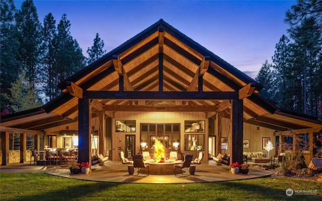 back house at dusk with an outdoor living space with a fire pit, a patio area, and a lawn