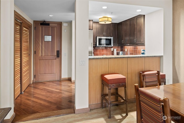 kitchen with kitchen peninsula, dark brown cabinets, decorative backsplash, a breakfast bar area, and stainless steel appliances