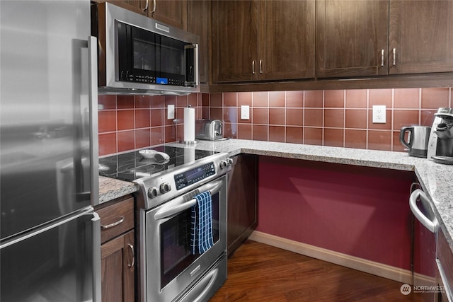 kitchen with light stone countertops, dark brown cabinetry, dark hardwood / wood-style flooring, backsplash, and stainless steel appliances