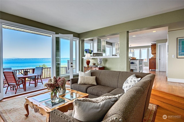 living area with a water view, plenty of natural light, baseboards, and wood finished floors