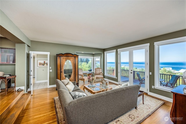 living room featuring light wood-style floors, french doors, a water view, and baseboards