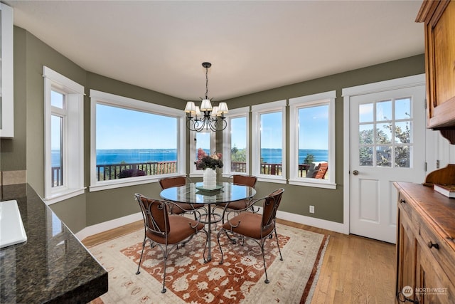 dining area featuring light wood-type flooring, a water view, baseboards, and an inviting chandelier