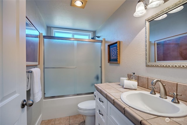 full bath featuring a textured wall, toilet, combined bath / shower with glass door, vanity, and tile patterned floors