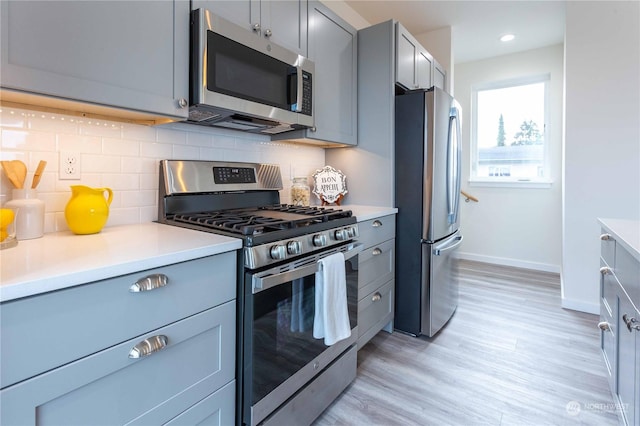 kitchen featuring backsplash, light hardwood / wood-style floors, gray cabinets, and stainless steel appliances