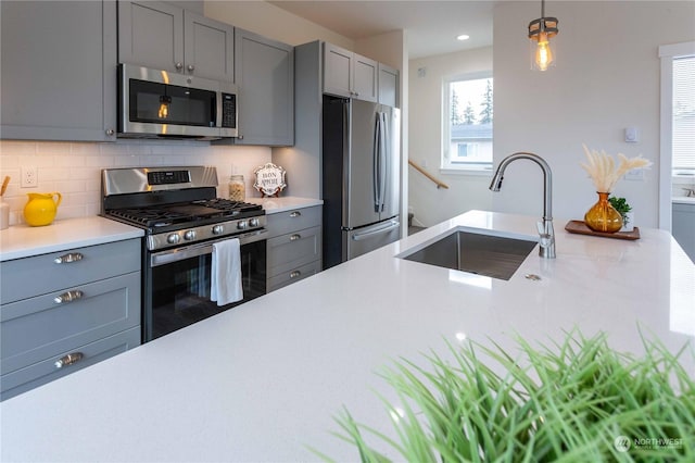 kitchen featuring gray cabinetry, pendant lighting, sink, tasteful backsplash, and stainless steel appliances