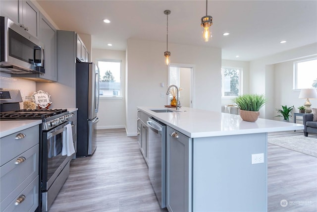 kitchen featuring appliances with stainless steel finishes, sink, a center island with sink, decorative light fixtures, and gray cabinets