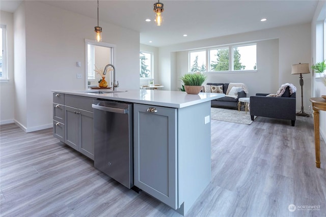 kitchen with gray cabinetry, a kitchen island with sink, sink, stainless steel dishwasher, and decorative light fixtures