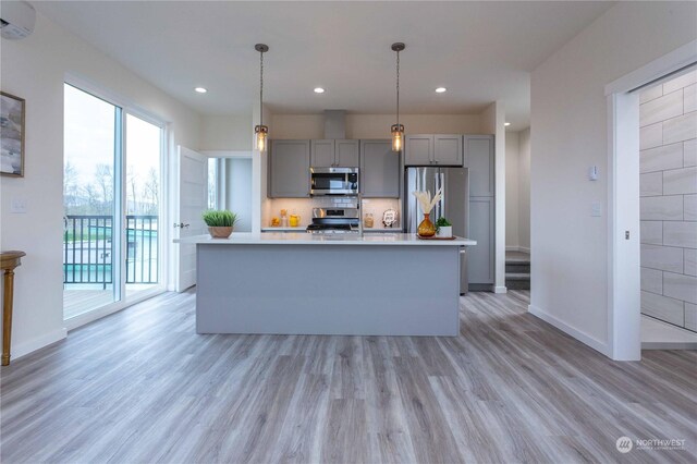 kitchen with gray cabinetry, a center island with sink, appliances with stainless steel finishes, and a wall mounted AC