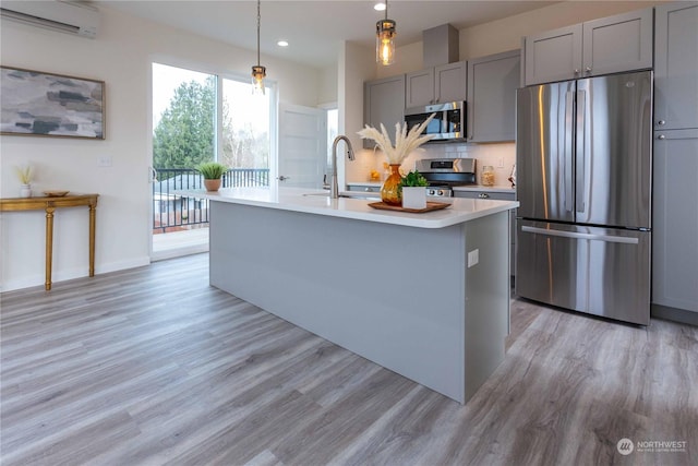 kitchen featuring a wall unit AC, gray cabinetry, a kitchen island with sink, and stainless steel appliances