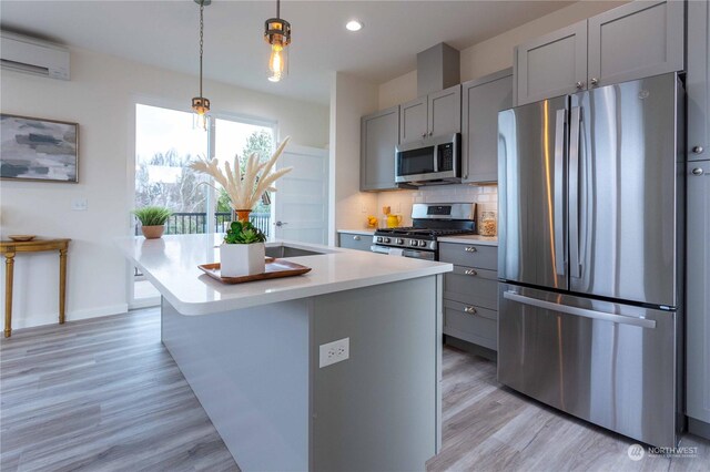 kitchen with pendant lighting, a center island with sink, decorative backsplash, gray cabinets, and stainless steel appliances