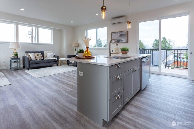 kitchen featuring a kitchen island with sink, sink, stainless steel dishwasher, decorative light fixtures, and light hardwood / wood-style floors