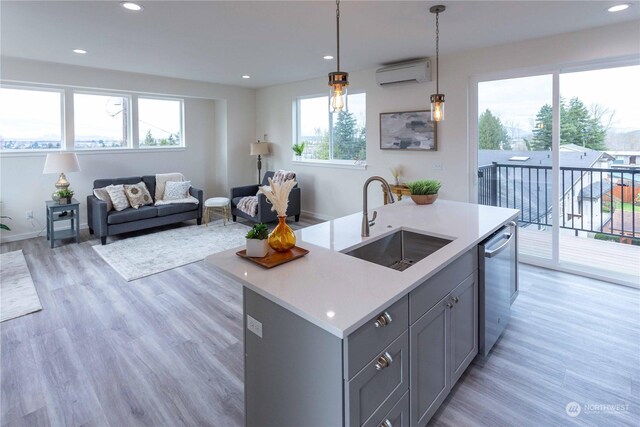 kitchen with stainless steel dishwasher, sink, decorative light fixtures, a center island with sink, and light hardwood / wood-style floors