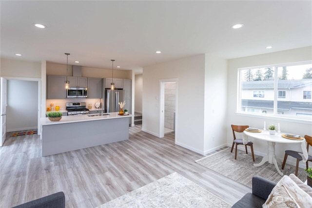 kitchen with a kitchen island with sink, light hardwood / wood-style flooring, gray cabinets, decorative light fixtures, and stainless steel appliances