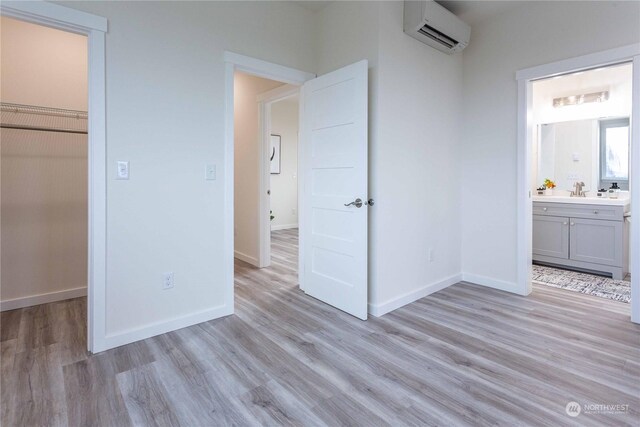 unfurnished bedroom featuring a walk in closet, ensuite bath, light hardwood / wood-style flooring, an AC wall unit, and a closet