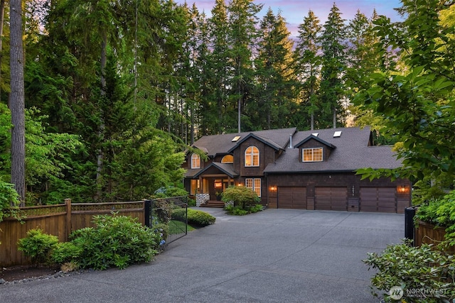 chalet / cabin with concrete driveway, an attached garage, fence, and a shingled roof