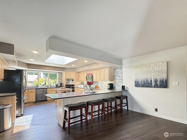 kitchen with a breakfast bar, tasteful backsplash, stainless steel appliances, a peninsula, and a skylight