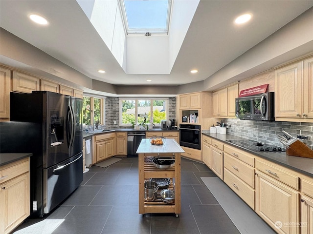 kitchen with a sink, black appliances, a skylight, and light brown cabinetry