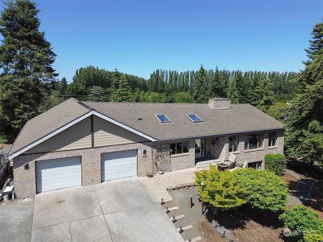 view of front facade with an attached garage, a shingled roof, concrete driveway, a view of trees, and brick siding