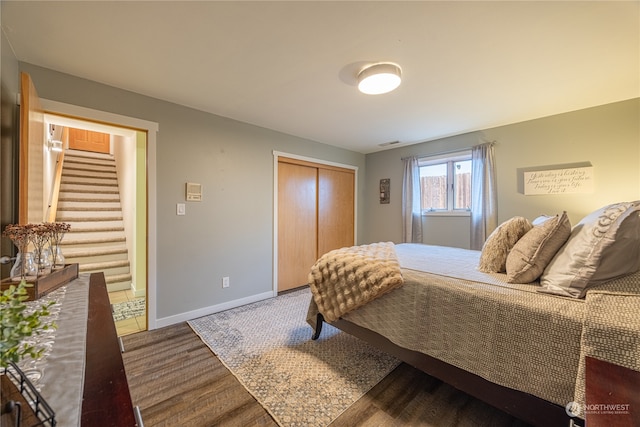 bedroom featuring wood finished floors, visible vents, baseboards, and a closet