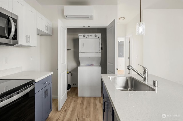kitchen featuring pendant lighting, stacked washer and dryer, sink, white cabinetry, and a wall unit AC