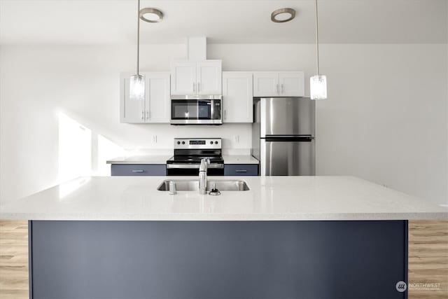 kitchen with appliances with stainless steel finishes, pendant lighting, sink, white cabinets, and light hardwood / wood-style flooring