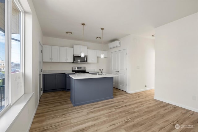 kitchen with a wall mounted AC, hanging light fixtures, appliances with stainless steel finishes, an island with sink, and white cabinets