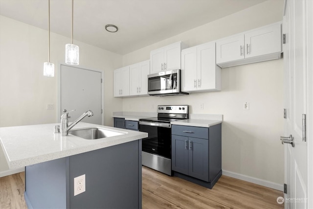 kitchen featuring appliances with stainless steel finishes, pendant lighting, white cabinetry, sink, and a kitchen island with sink